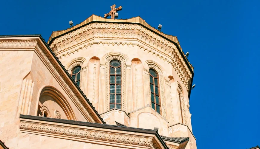 Close-up view of the central dome and facade of the Holy Trinity Cathedral (Sameba) in Tbilisi, Georgia, under a clear blue sky.