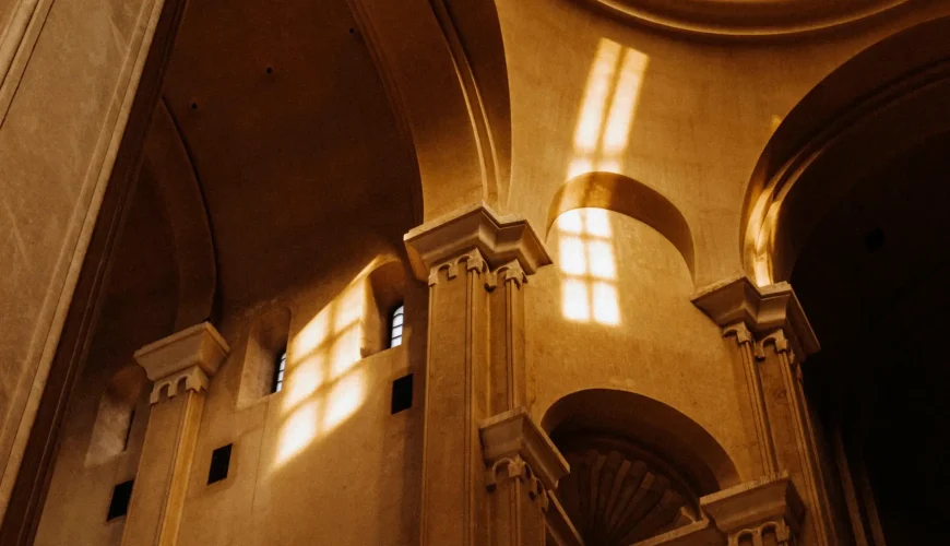 A high-angle interior shot of the Holy Trinity Cathedral (Sameba) in Tbilisi, with light streaming through arched windows and illuminating the large, arched pillars.