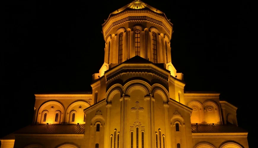 The front facade of the Holy Trinity Cathedral (Sameba) in Tbilisi, brilliantly illuminated at night against a dark sky.