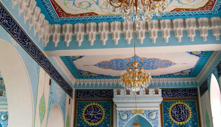 Interior of the Jumah Mosque in Tbilisi, with beautifully decorated blue, white, and gold ceilings and walls, and two chandeliers.