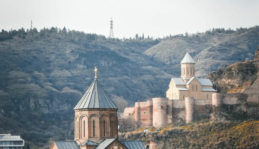 A beautiful view of two historic churches on a hillside in Tbilisi Old Town, with the hills and a power line in the background.