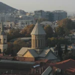 Rooftop view of the Sioni Cathedral in Tbilisi, Georgia, with its distinctive dome and surrounding Old Town architecture and modern buildings in the distance.