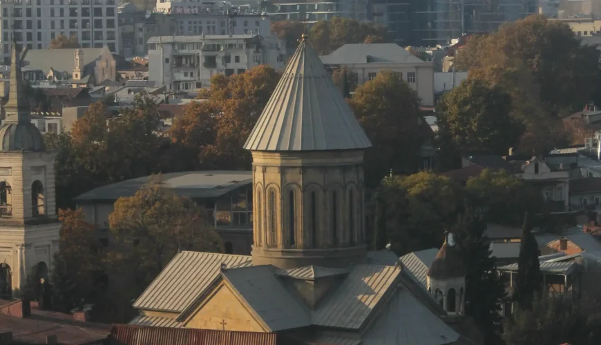Rooftop view of the Sioni Cathedral in Tbilisi, Georgia, with its distinctive dome and surrounding Old Town architecture and modern buildings in the distance.