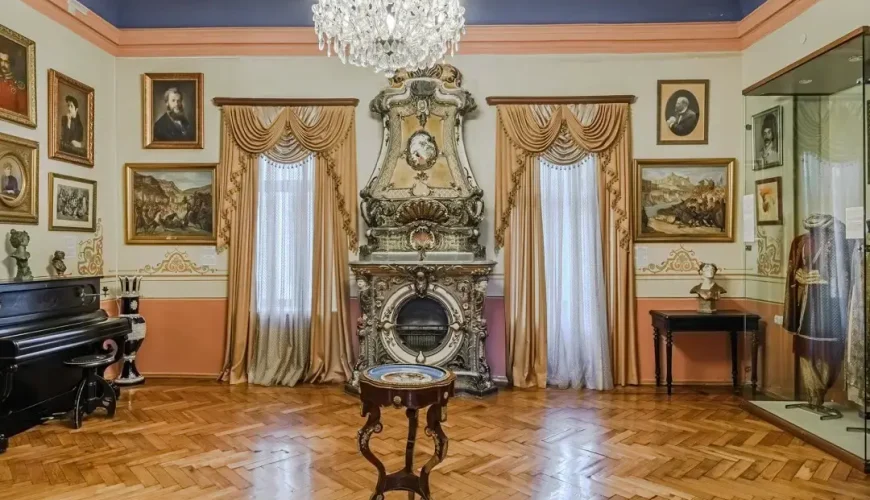 A lavish hall inside the Art Palace of Georgia (Museum of Cultural History) in Tbilisi, with a grand chandelier, an ornate fireplace, multiple framed portraits, and intricate wall decorations.