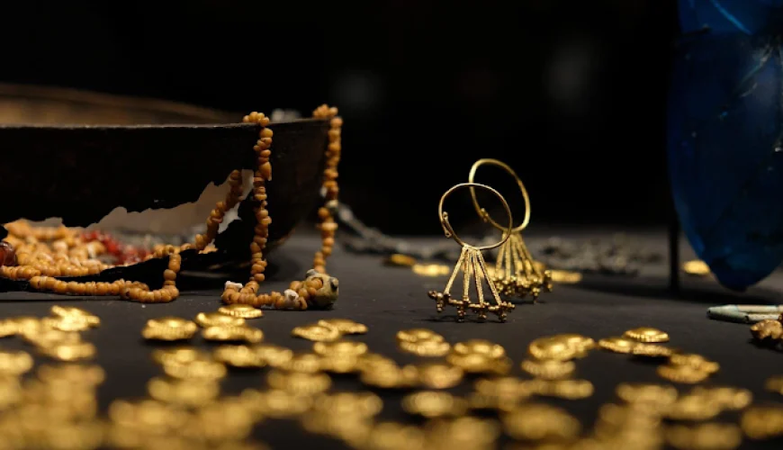 A close-up of intricate ancient gold jewelry and small gold artifacts displayed on a dark surface, part of the valuable collection at the Georgian National Museum in Tbilisi.