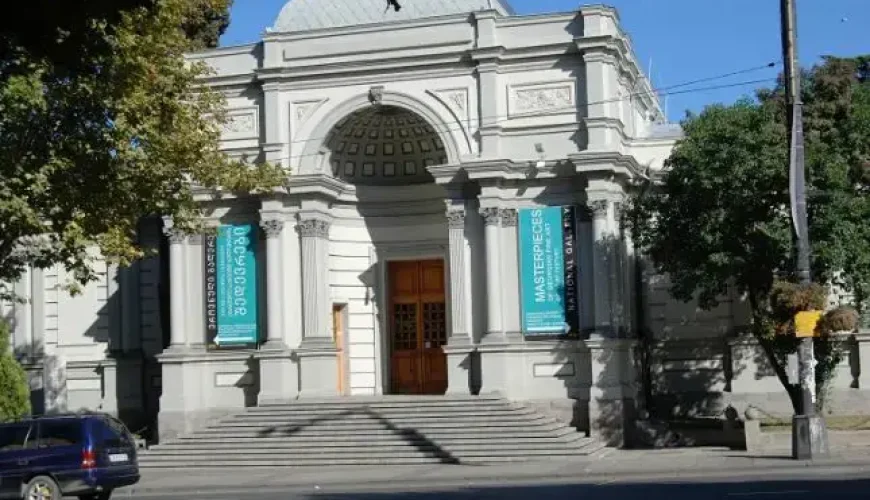 The grand classical facade of the National Gallery (Blue Gallery) in Tbilisi, Georgia, with its large arched entrance, prominent staircase, and banners advertising 'MASTERPIECES OF GEORGIAN FINE ART'