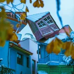 Traditional colorful wooden balconies with intricate carvings on snow-dusted buildings in Tbilisi's Old Town, with yellow leaves in the foreground.
