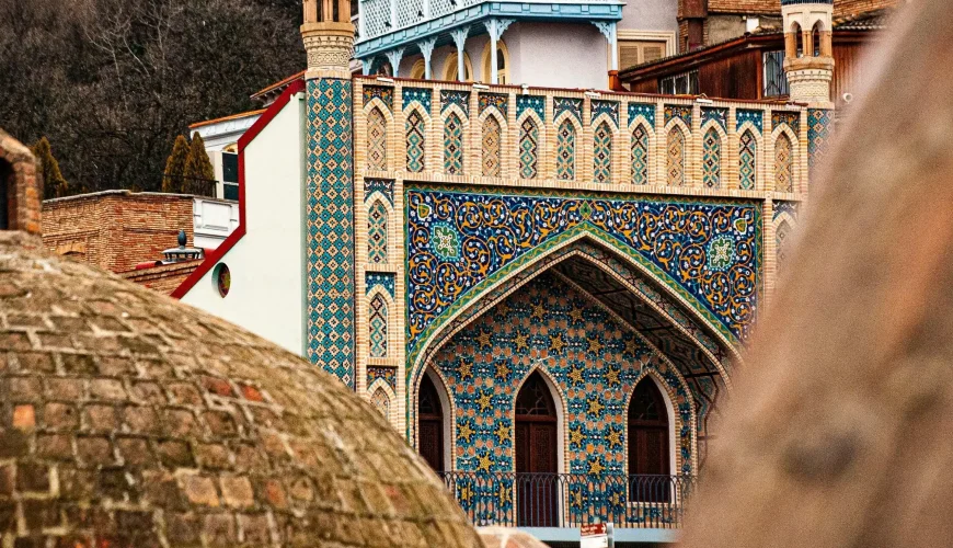 View of the ornate Chreli Abano (Orbeliani) sulfur bathhouse and a traditional building, with domed bathhouse roofs and old town architecture in the foreground.