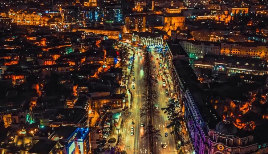 Aerial view of Rustaveli Avenue in Tbilisi at night, with streetlights illuminating the boulevard and a distant mountain with a lit TV tower.
