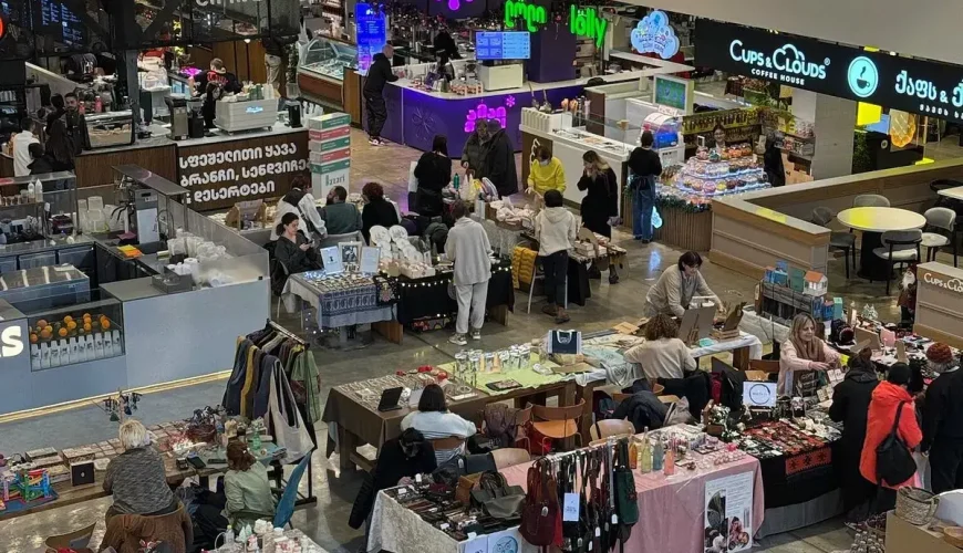 An overhead view of a lively indoor market with people shopping at stalls selling crafts, jewelry, and other unique goods