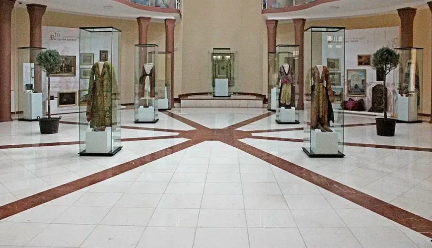 The bright, spacious main exhibition hall of the David Baazov Museum of History of Jews of Georgia in Tbilisi, featuring display cases with historical garments and artifacts, set on a tiled floor with radiating lines.