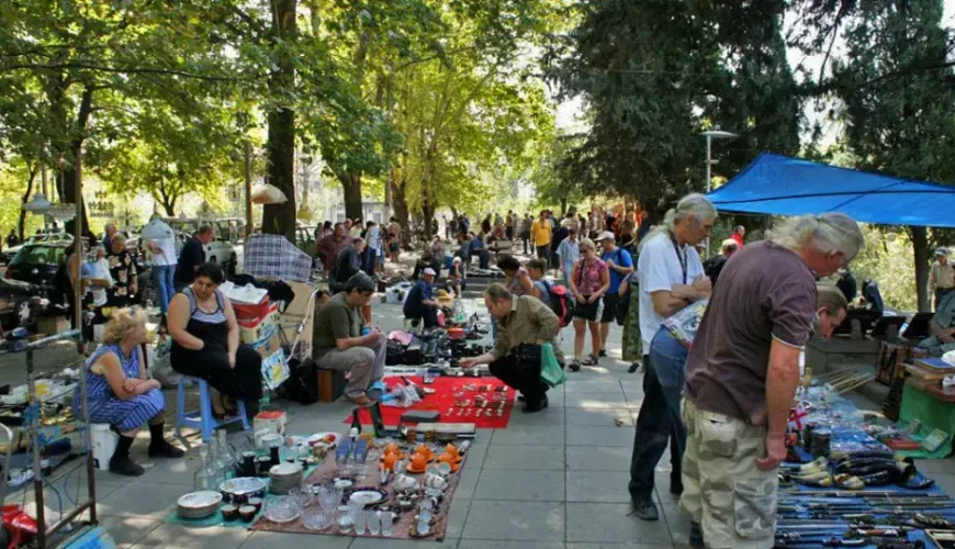 A bustling outdoor flea market in Tbilisi under a canopy of trees, with vendors and shoppers Browse various antiques and goods