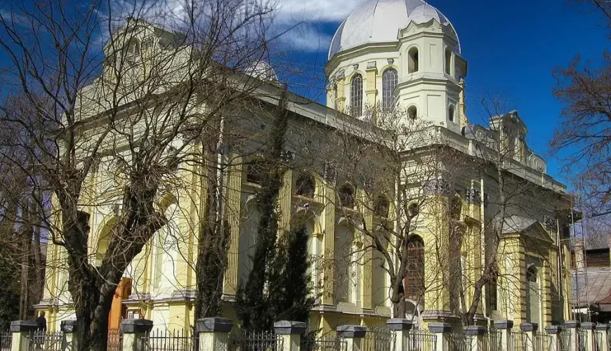 The stately yellow and white facade of the Georgian Medicine History Museum in Tbilisi, Georgia, featuring a prominent dome and classical architectural details, framed by bare trees.