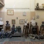 An interior view of the Iakob Nikoladze Museum in Tbilisi, Georgia, showcasing a collection of plaster and bronze busts, sculptures, and various art tools, resembling an artist's studio.