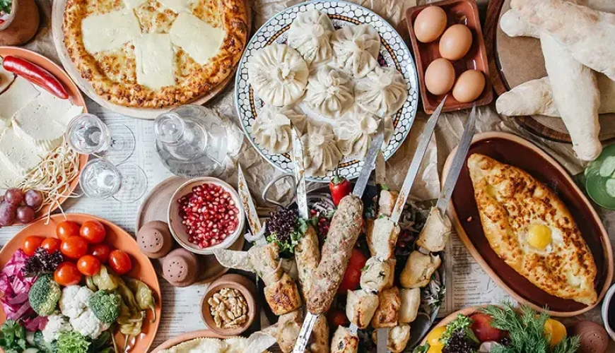 A lavish spread of traditional Georgian dishes on a table, including Khachapuri, Khinkali, Mtsvadi kebabs, fresh vegetables, cheese, and bread, likely from the Museum of Culinary Recipes in Tbilisi.
