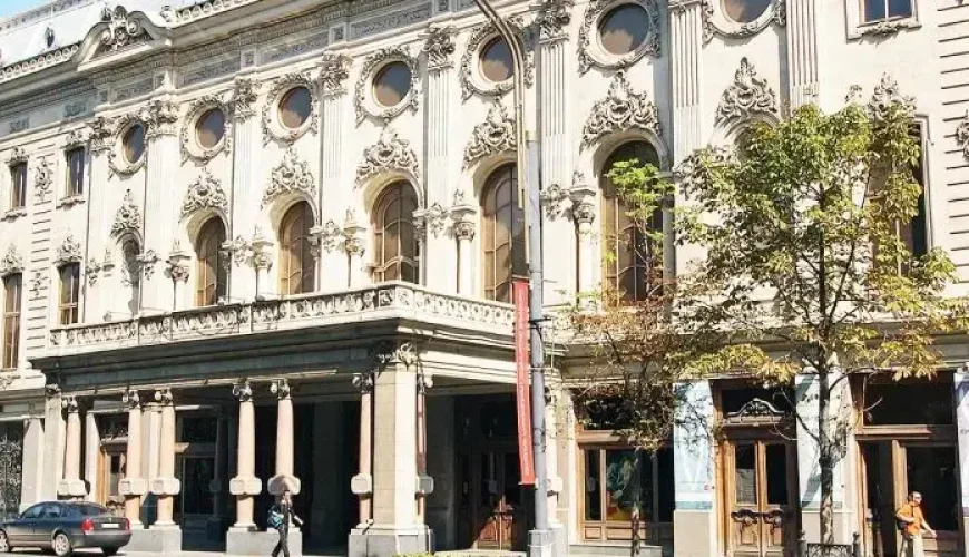 The ornate white facade of the Rustaveli National Theatre, a 19th-century building in Rococo style with a balcony and tall arched windows