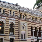 The ornate exterior of the Tbilisi Opera and Ballet Theatre with a yellow and striped facade, arched windows, and decorative lanterns