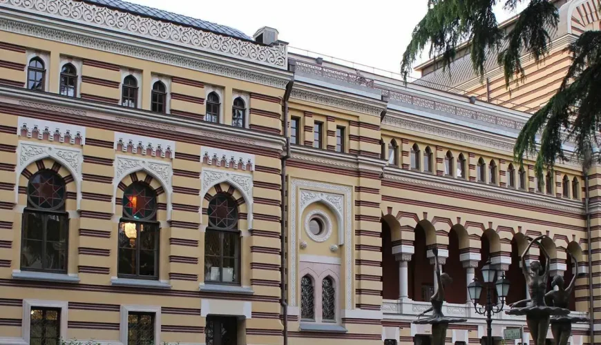 The ornate exterior of the Tbilisi Opera and Ballet Theatre with a yellow and striped facade, arched windows, and decorative lanterns